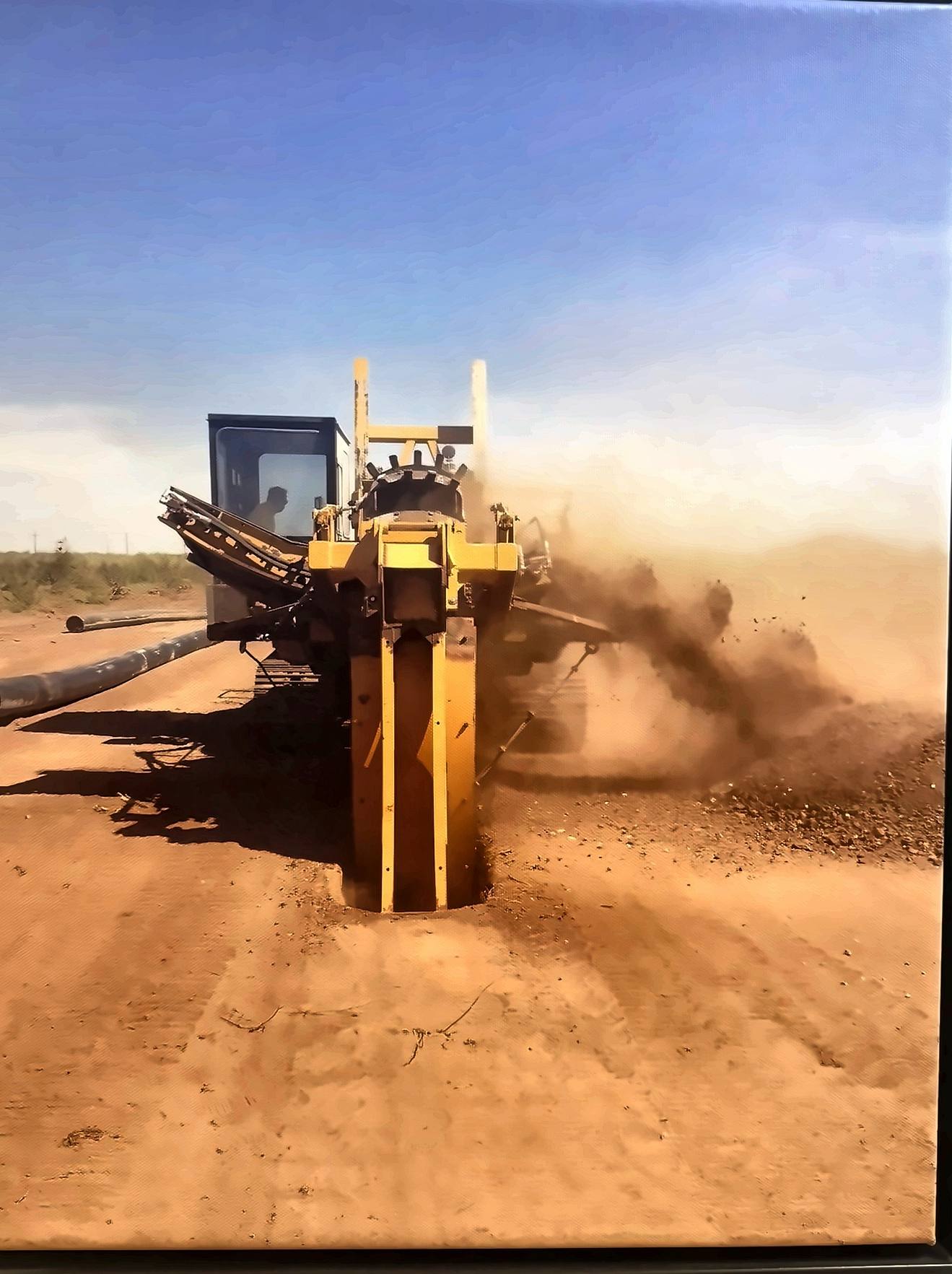 Encore trencher cutting a pipeline ditch through dusty caliche