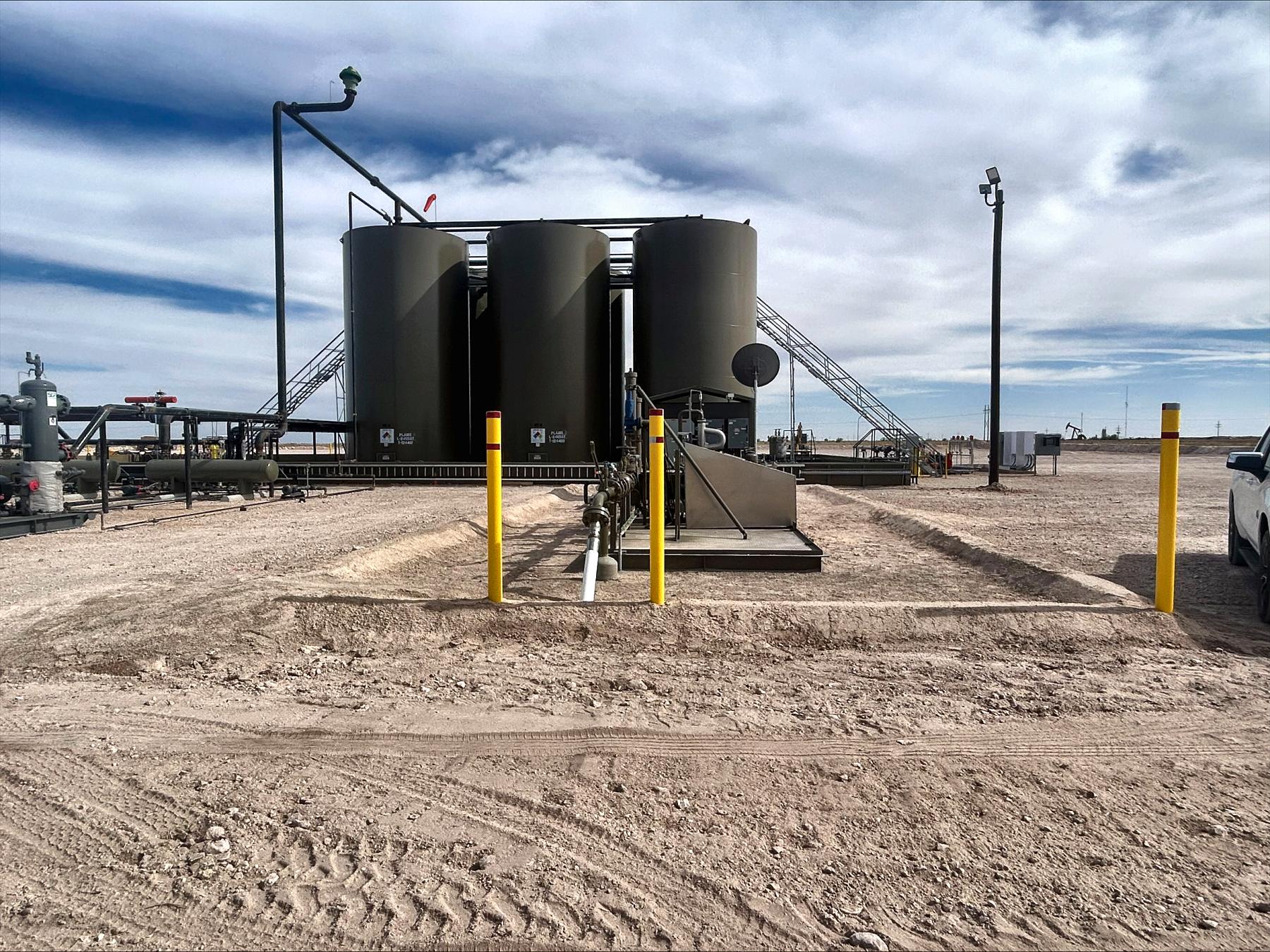 Tank battery with storage tanks, a separator and piping behind yellow safety bollards