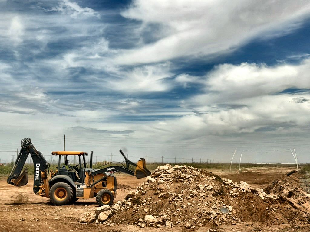 Backhoe working caliche spoil on a pipeline right-of-way